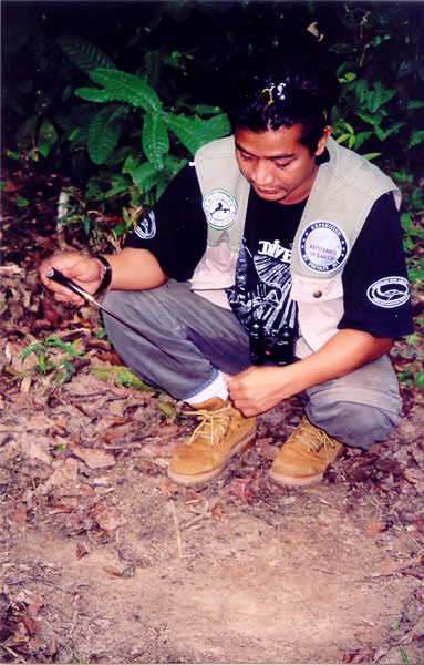 Zuan points to elephant's footprint with his hunting knife